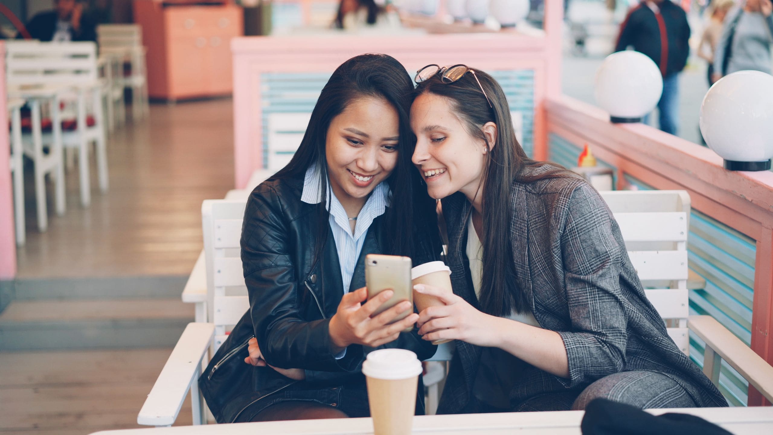 Two friends smiling over coffee and a phone