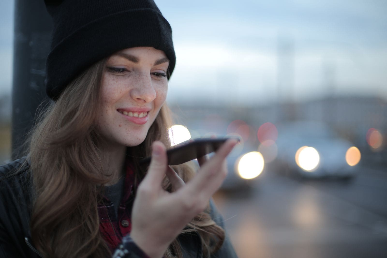 Woman smiling with her phone on a city street at dusk