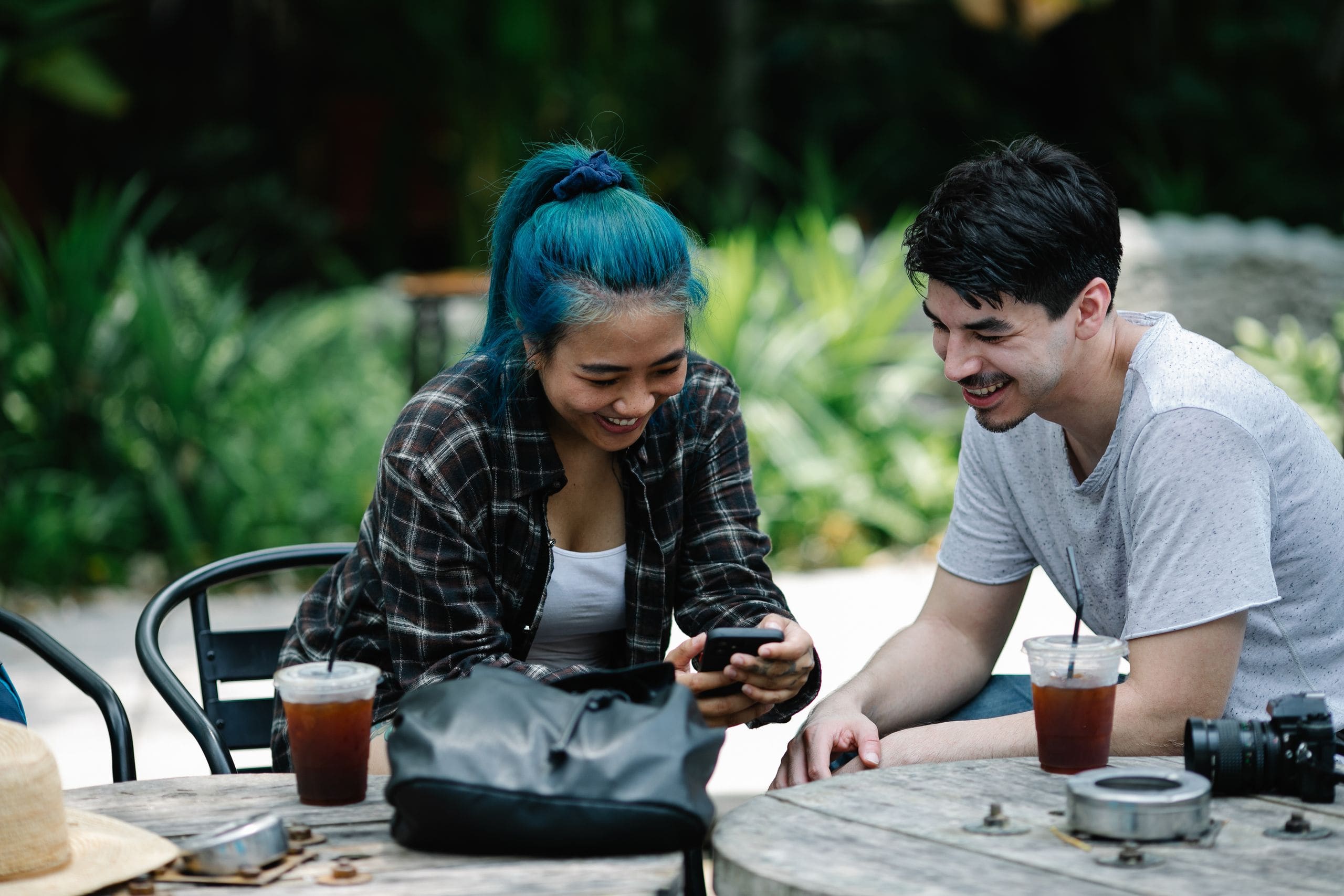 Two friends smiling over a phone at an outdoor café
