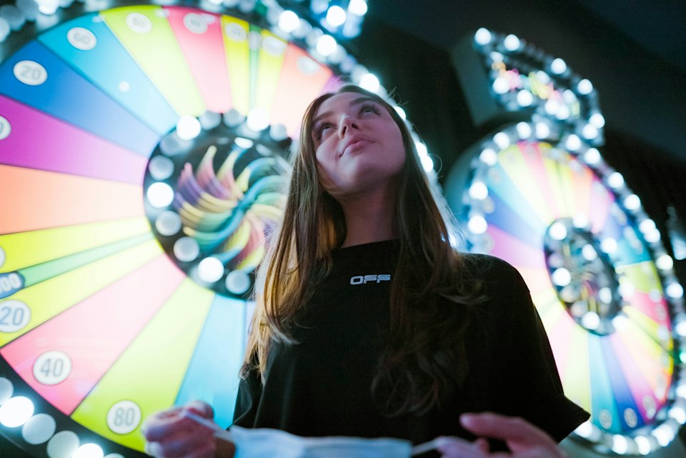 A woman standing in front of a lit-up prize wheel